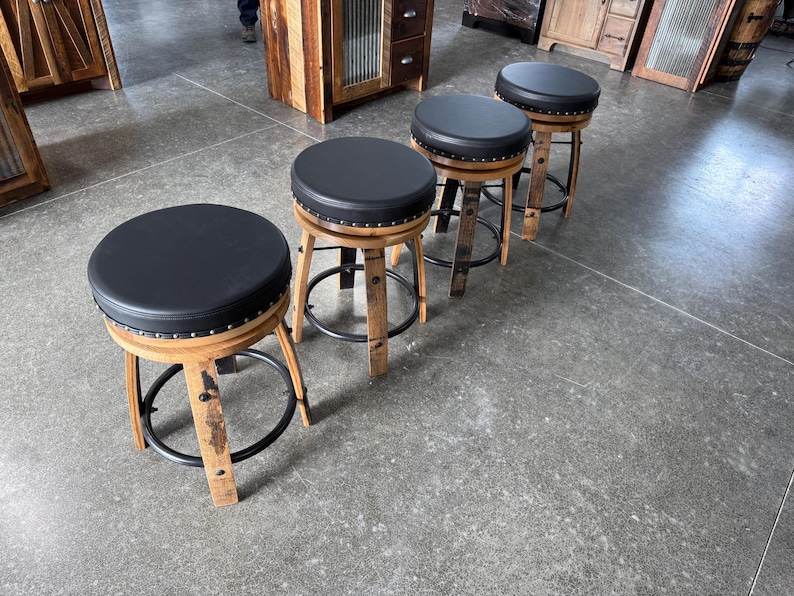 May include: A set of four bar stools featuring round black padded seats with silver nailhead trim. The bases are constructed from curved light brown wood staves with a circular black metal footrest connecting the legs of each stool.
