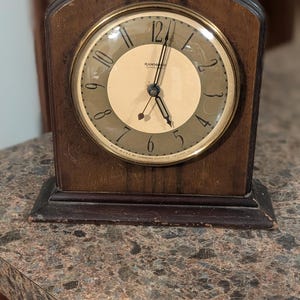 May include: An antique wooden clock with a round face and gold-colored trim. The clock face is cream-colored with black numerals and hands. The clock is marked "HAMMOND" and "MADE IN U.S.A. BY HAMMOND CLOCK CO. CHICAGO USA."