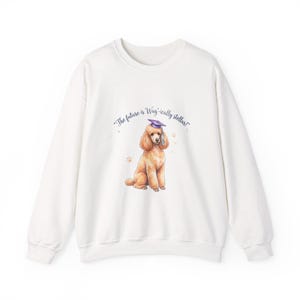 Puede incluir: Sudadera blanca con una ilustración de acuarela de un caniche con birrete. El texto "The future is Wag-ically stellar!" está impreso encima del perro. Huellas de patas están dispersas alrededor del perro.