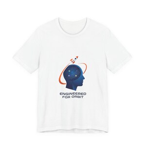 Puede incluir: Camiseta blanca con la silueta azul de una cabeza que contiene un diseño de galaxia, una órbita naranja y un cohete. El texto "ENGINEERED FOR ORBIT" está impreso debajo.
