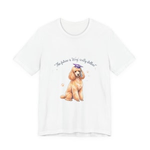 Puede incluir: Camiseta blanca con una ilustración en acuarela de un caniche con birrete. El texto "The future is Wag-ically stellar!" está impreso encima del perro. También son visibles huellas de patas.