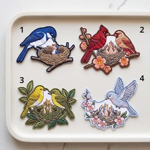 May include: Four embroidered patches featuring bird families in nests. Patch 1 shows a blue bird with a chick. Patch 2 features red and brown birds with three chicks and flowers. Patch 3 displays yellow and green birds with chicks. Patch 4 shows a light blue bird with chicks and pink flowers.