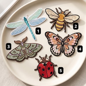 May include: Five embroidered insect and butterfly patches labeled 1 through 5. Patch 1 is a blue dragonfly, 2 is a brown and yellow bee, 3 is a green moth, 4 is an orange and black butterfly, and 5 is a red ladybug with black spots.