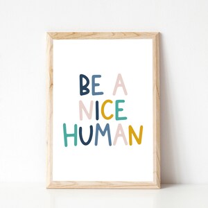 May include: A framed print with the text "BE A NICE HUMAN" in colorful, stylized lettering. The letters are in shades of blue, green, pink, and yellow.