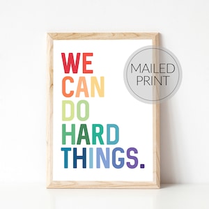 May include: A framed print with the text "WE CAN DO HARD THINGS." in rainbow colors. The print is in a light wood frame and has a white background.