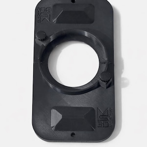 Puede incluir: Un objeto rectangular negro impreso en 3D con una abertura circular en el centro. El objeto tiene dos secciones rectangulares elevadas y dos pequeños botones. El texto "MS 3D" es visible.