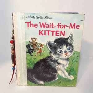 Puede incluir: Un libro Little Golden Book titulado The Wait-for-Me Kitten, con una ilustración de un gatito blanco y negro en la portada, y un dije de cuentas decorativo unido al lomo con cordones de cuero rojo y varias cuentas de colores.