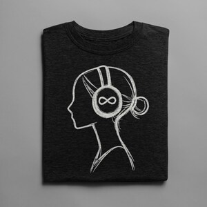 May include: Dark gray t-shirt featuring a white line drawing of a person's profile wearing headphones with an infinity symbol on the ear cup. The person's hair is styled in a bun. The t-shirt is folded neatly on a gray surface.