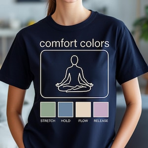 May include: Navy blue t-shirt with the words "comfort colors" and a white graphic of a person in a seated yoga pose. Below the graphic are four colored squares with the words "STRETCH", "HOLD", "FLOW", and "RELEASE".