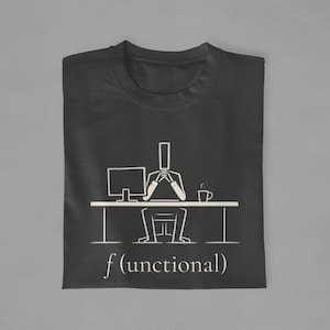 May include: Black t-shirt with a white graphic of a person sitting at a desk with a computer and a coffee cup. The text "f(unctional)" is printed below the graphic. The shirt is folded on a gray surface.