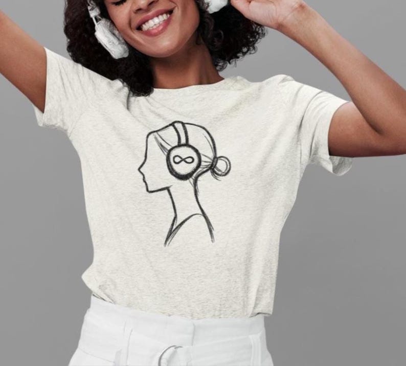 May include: A light grey t-shirt with a black line drawing of a woman's profile wearing headphones with an infinity symbol on the earcups. The design is centered on the shirt.