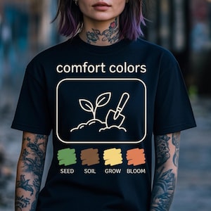 May include: Black t-shirt featuring the words "comfort colors" above a white outline of a plant, soil, and trowel. Below are colour swatches labelled "SEED", "SOIL", "GROW", and "BLOOM".