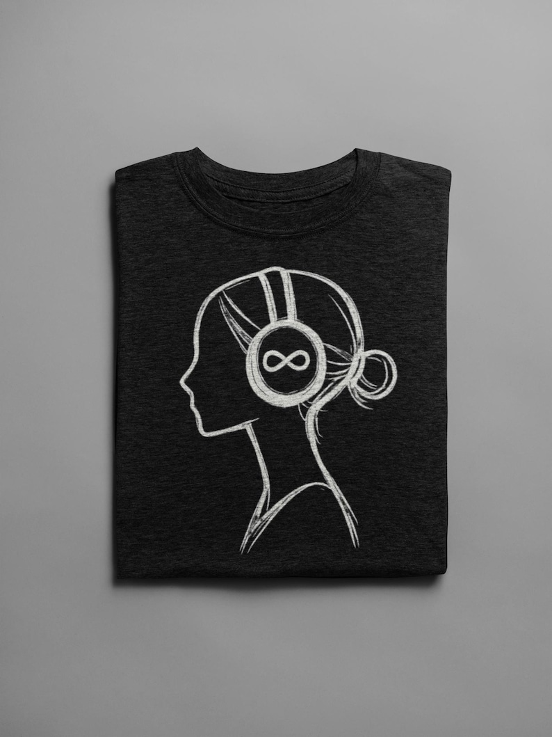 May include: Dark gray t-shirt featuring a white line drawing of a person's profile wearing headphones with an infinity symbol on the ear cup. The person's hair is styled in a bun. The t-shirt is folded neatly on a gray surface.