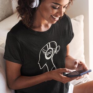 May include: Black t-shirt featuring a white graphic of a person's profile wearing headphones with an infinity symbol. The person is holding a smartphone. The t-shirt is a crew neck style.