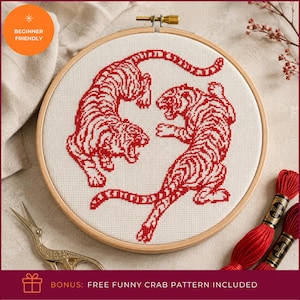 May include: A circular wooden embroidery hoop containing white fabric with a red cross-stitch design of two tigers facing each other. The tigers are depicted in a dynamic pose with striped patterns. Two skeins of red embroidery thread are included.