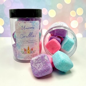 May include: A clear plastic jar with a black lid containing pink, purple, and blue sugar scrub cubes. The label reads Fizz & Fable Unicorn Scrubbies, Mystical Sugar Scrub Cubes, Sweetly Scented & Brightly Colored, Net Wt. 6 oz (170 g).