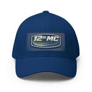 May include: A navy blue baseball cap with a curved brim. The cap features an embroidered patch with the text "12th MC" in white, outlined in silver, with green and blue accents.