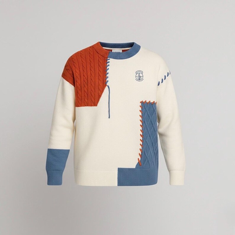 以下が含まれることがあります： オレンジ色のケーブルニットとブルーのアクセントが特徴のクリーム色のセーター。オレンジとブルーのステッチパッチと胸元の小さなエンブレムが特徴的なユニークなデザインです。袖口はブルーです。