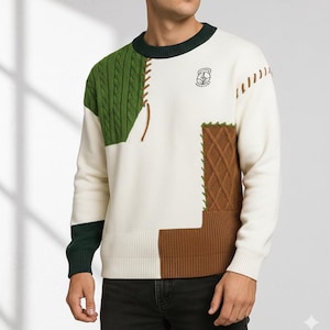 Può includere: Maglione color crema con design a blocchi di colore verde e marrone. Presenta un pannello a trecce, un motivo a rombi e dettagli cuciti. Include un piccolo stemma sul petto e finiture verde scuro.