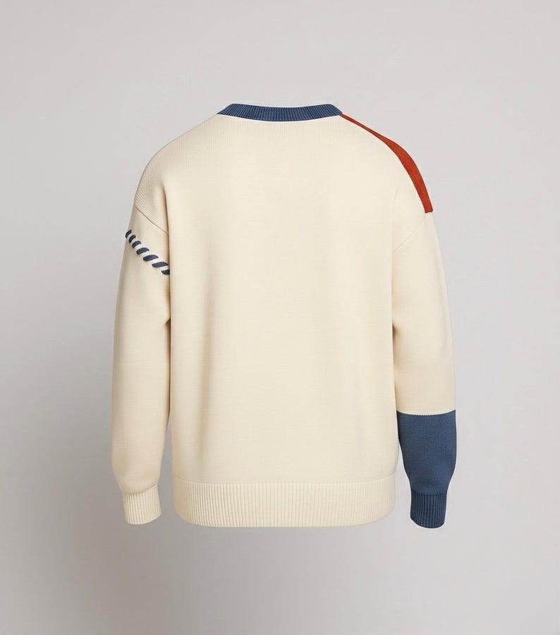 以下が含まれることがあります： クリーム色のセーター。青と錆色のアクセントが特徴。青いネックライン、肩の錆色のストライプ、袖口の青いカフス。左袖には装飾的なステッチデザインがあります。