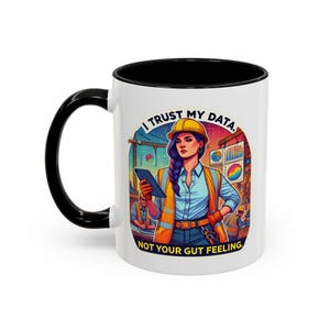 May include: White ceramic mug with a black interior and handle. The mug features a colourful illustration of a woman in construction attire holding a tablet, with the text "I TRUST MY DATA, NOT YOUR GUT FEELING."