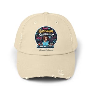 Peut inclure: Casquette de baseball beige délavé avec un motif circulaire représentant une femme devant un ordinateur portable, avec le texte "Fluent in Sarcasm, Schematics & Stress". Le texte "Strength & Stilettos" est en dessous.