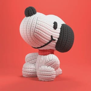 Może przedstawiać: Dzianinowa figurka Snoopy w pozycji siedzącej. Postać jest głównie biała z czarnymi akcentami na uszach, nosie i oczach. Czerwony szalik wokół szyi, na jednolitym czerwonym tle.