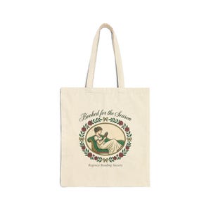 Peut inclure: Sac fourre-tout crème avec un dessin d'une femme lisant, entourée d'une couronne florale. Le texte "Booked for the Season" et "Regency Reading Society" sont imprimés sur le sac. Le sac a deux poignées.
