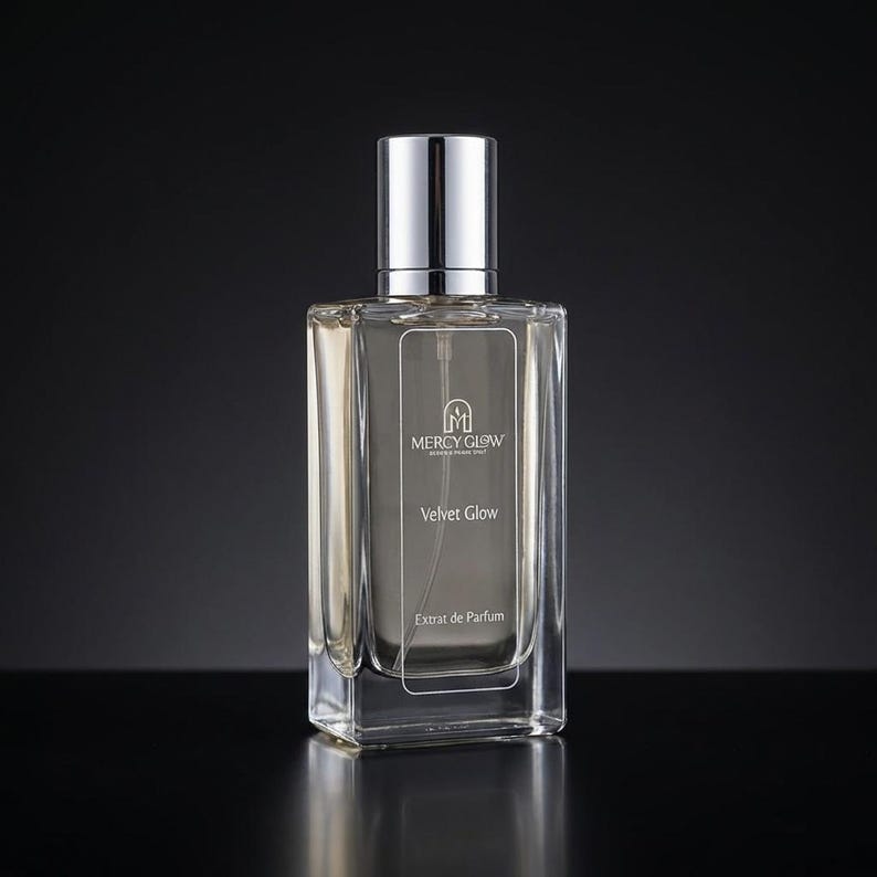 May include: A rectangular glass perfume bottle with a silver cap. The bottle has a clear liquid inside and features the text "MERCY GLOW" and "Velvet Glow" in white. The words "Extrait de Parfum" are also visible.