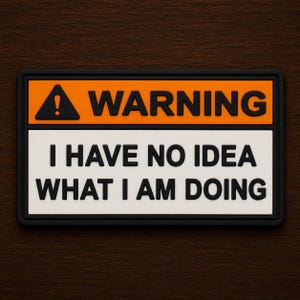 May include: A rectangular patch with a black border. The top section is orange with the word "WARNING" in black. Below, a white section reads "I HAVE NO IDEA WHAT I AM DOING" in black, with a black exclamation point symbol.
