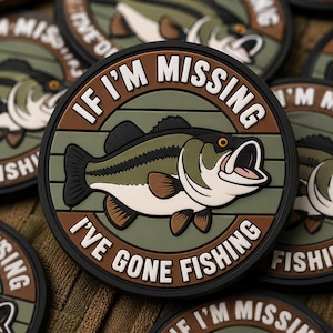 May include: Circular patch with a cartoon bass fish illustration. The patch has a black border, brown and green accents, and the text "IF I'M MISSING I'VE GONE FISHING" in white.