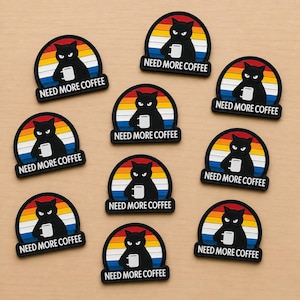 May include: A collection of black cat patches, each holding a white mug, set against a colorful sunset design. The text "NEED MORE COFFEE" is displayed below each cat. The patches are arranged on a light brown surface.
