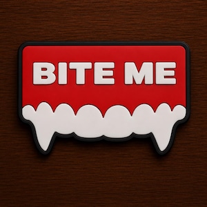 May include: A rectangular patch with a black border, featuring a bright red background and the white text BITE ME. Below the text, a white graphic element resembles a row of vampire teeth with two prominent fangs extending downwards.