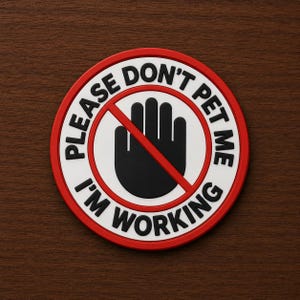 May include: A circular patch with a white background and a red border. In the center is a black hand icon crossed out by a red diagonal line. The black text around the border reads, PLEASE DON'T PET ME I'M WORKING, in a bold, sans-serif font.