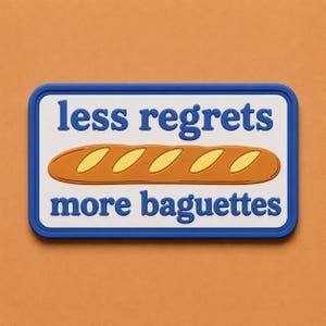 May include: A rectangular sign with a blue border and the words "less regrets" above "more baguettes" in blue text. A brown baguette with yellow accents is in the center of the sign.
