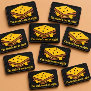 May include: A collection of black rectangular patches featuring a grilled cheese sandwich design. The sandwich is yellow and brown with melted cheese. The text "I'm make'n em at night" is printed in white on each patch.