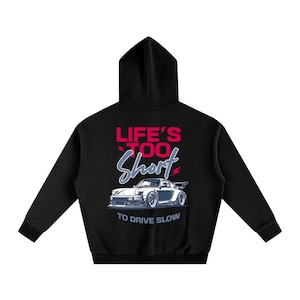 Puede incluir: Sudadera con capucha negra con un gráfico de un coche deportivo blanco y el texto "LIFE'S TOO SHORT TO DRIVE SLOW" en rojo y azul. La sudadera tiene capucha y mangas largas.