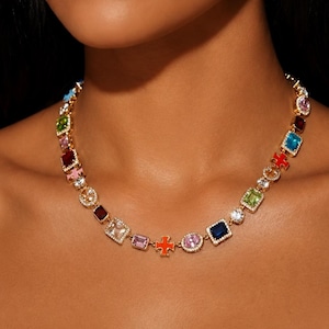 May include: A gold-tone chain necklace featuring a series of multi-colored, multi-shaped gemstones and charms. The stones include various cuts such as emerald, round, and square, in hues of blue, pink, green, red, and clear, set in gold metal.