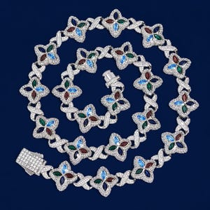 May include: A silver-toned necklace with a repeating floral design. Each flower has four petals, each with a different colored gem: red, blue, green, and clear. The necklace is on a dark blue background.