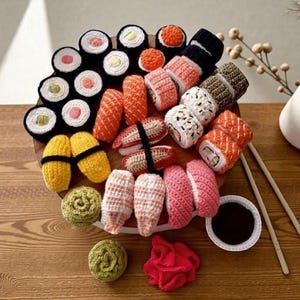 Może przedstawiać: Kolekcja szydełkowego sushi ułożona na drewnianej tacy. Sushi, w kolorach pomarańczowym, różowym, białym i zielonym, obejmuje różne rodzaje, takie jak maki i nigiri. Mała miseczka sosu sojowego i pałeczki dopełniają całość.