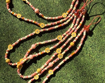 May include: Several beaded phone charms in shades of pink, yellow, and white. Each charm features small, colorful beads and decorative yellow flower accents. The charms have a loop at the top for attaching to a phone or other device.