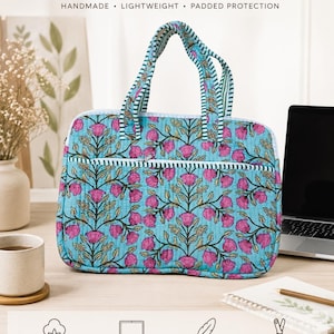 May include: A quilted laptop cover featuring a light blue background with a repeating pink floral and green leaf pattern. It includes two handles with green and white stripes, a front zipper pocket, and text reading Quilted Laptop Cover.