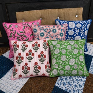 Puede incluir: Una colección de cinco cojines cuadrados con diversos estampados florales en bloques de colores vibrantes como rosa, azul, verde y rojo. Cada cojín está rematado con un borde ribeteado a juego, mostrando motivos botánicos.