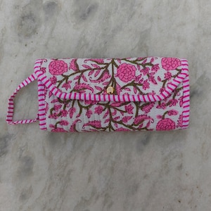 Könnte beinhalten: Eine rechteckige, gesteppte Clutch mit weißem Untergrund und einem Blockdruckmuster aus rosa Blüten und grünen Ranken. Die Geldbörse hat einen Klappverschluss mit goldenem Druckknopf und ist mit rosa-weiß gestreiftem Stoff eingefasst.