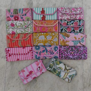 May include: A collection of rectangular quilted fabric wallets featuring various patterns including floral, striped, leopard, and botanical prints. Each wallet has a flap closure with a single gold-tone snap button and contrasting stitched edges.