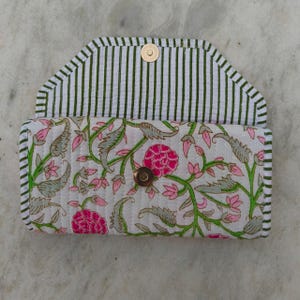 Op de afbeelding: Een gewatteerde stoffen clutch portemonnee met een witte basis en een roze en groen bloemenrankpatroon. De binnenflap heeft een verticaal gestreept ontwerp in groen en wit. Een enkele goudkleurige metalen drukknoop sluit de voorzijde af.