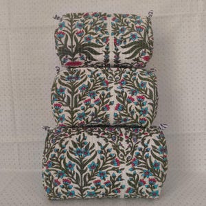 Peut inclure: Un ensemble de trois pochettes en tissu rectangulaires empilées, présentant une base blanche avec un motif floral répétitif dans des tons de vert, bleu et rose. Chaque pochette a une texture matelassée et de petites boucles en tissu.