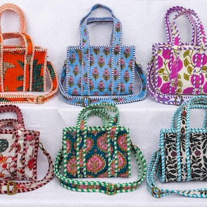 Op de afbeelding: Zes rechthoekige gewatteerde draagtassen met handvatten en verstelbare schouderbanden. Elke tas heeft een uniek bloemen- of dierenpatroon in levendige kleuren zoals oranje, blauw, roze, wit, groen en zwart met een gestreepte afwerking.