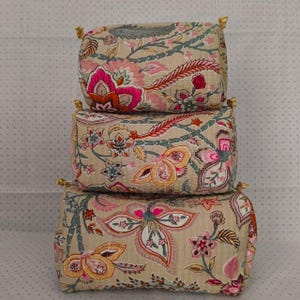 Peut inclure: Une pile de trois pochettes rectangulaires en tissu matelassé de tailles différentes. Chaque pochette présente un fond beige avec un motif floral répétitif dans des tons de rose, orange, bleu sarcelle et vert foncé, avec des languettes jaunes.