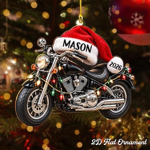 May include: A flat, two-dimensional Christmas tree ornament shaped like a black motorcycle. The motorcycle is adorned with colorful string lights and features a red Santa hat resting on the handlebars. The hat displays the name MASON and the year 2026.